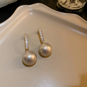 Detailed view of gold pearl earrings with zircon stones on a beige ceramic tray