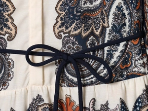 Detailaufnahme des Kleides mit Paisley-Muster in Cremeweiß und dunkelblauer Bindeschleife