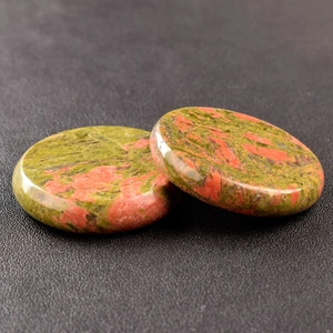 Detailed macro view of two polished Unakite crystal stones on a textured black surface