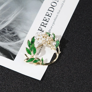 Detailed macro view of golden flower wreath brooch with green enamel and white pearls