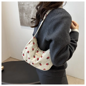 Detail of white corduroy underarm bag featuring red strawberry prints and gold tag