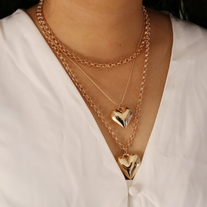 Chic multi-layer gold necklace featuring heart pendants on a female model in white shirt