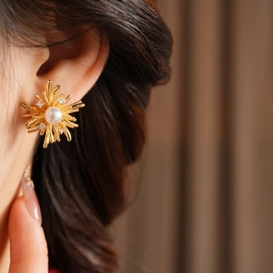 Close-up of gold flower stud earring with pearl center and sparkling zircon stones