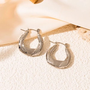 Macro detail of silver titanium steel earrings with textured grooves on stone pedestal