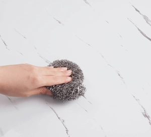 Self-adhesive oil-proof kitchen sticker being wiped clean with a metal scrubber