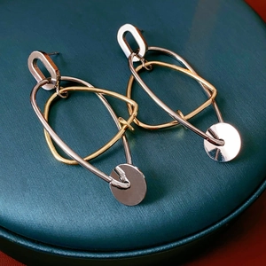 Détail de boucles d'oreilles bicolores dorées et argentées sur un écrin à bijoux vert foncé