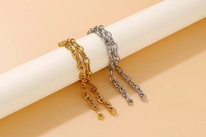 Polished gold and silver pig nose link chains hanging on a minimalist white cylinder