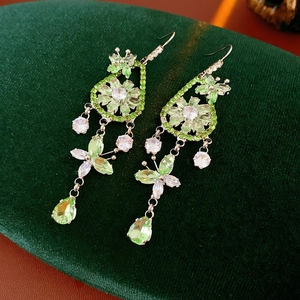 Macro shot of silver flower and butterfly drop earrings with green crystals on velvet