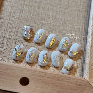 Dettaglio di unghie finte di lusso con farfalle dorate e perle in stile francese