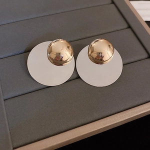 Detailed view of silver sequin stud earrings with gold spherical accents on grey leather