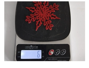 Detail shot of a 10cm red glitter snowflake ornament weighing 6g on a digital scale