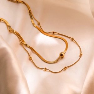 Minimalist gold double-layered necklace featuring snake and bead chains with metallic beads