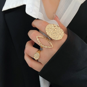 Close-up of three-piece gold vintage textured rings worn on model against black background