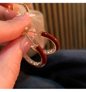 Close-up of red enamel C-shaped earrings with rhinestones in 14K gold plating