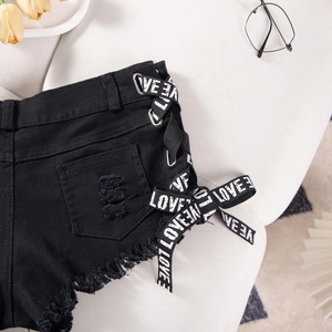 Dettaglio di pantaloncini di denim neri strappati con nastro LOVE e orlo a frange