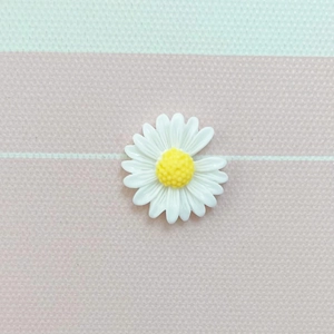Detailed view of a white resin daisy flower charm for DIY crafts on a striped surface