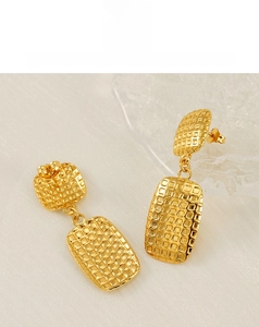 Macro detail of gold-plated square grid patterned drop earrings on white fabric