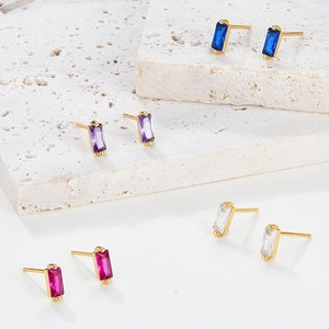 Macro shot of colorful baguette-cut zircon stud earrings on textured white stone display