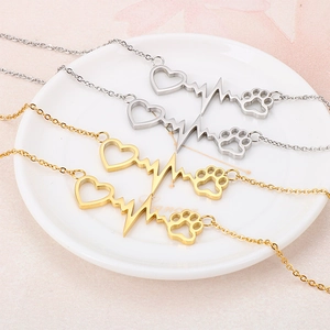 Goldenes und silbernes Edelstahl-Armband mit Herz- und Katzenpfoten-Anhänger auf Tablett