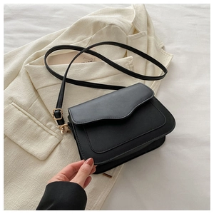Detail of black envelope crossbody bag with gold buckle on a beige blazer background