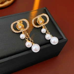 Macro view of gold rose earrings with zircon inlay and triple pearl drops on jewelry box