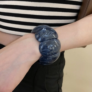 Detail of wide acrylic bracelet featuring blue marble pattern on female wrist