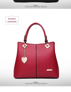 Detail view of wine red tote bag with gold heart pendant and vertical stitching