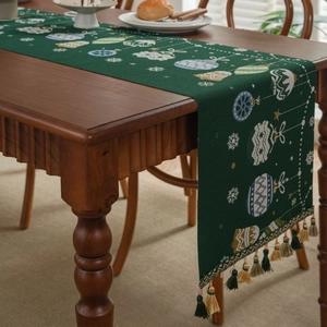 Macro detail of dark green Christmas table runner with festive patterns and tassels