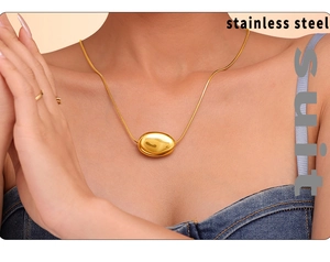 Detail of a polished gold bean pendant on a stainless steel necklace worn on the neck