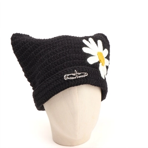 Detail of black knit cat ear beanie with daisy embroidery and metal safety pin accessory