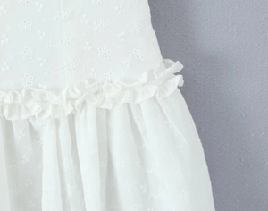 Close-up of white embroidered dress showing intricate floral patterns and ruffle waist detail