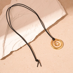 Detail of creative spiral gold pendant with black cord on a minimalist stone background