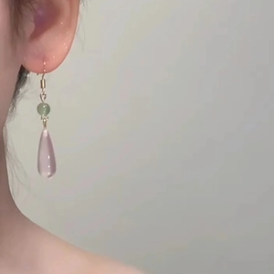 Pink resin teardrop earrings with green beads and gold hooks worn in a close-up shot