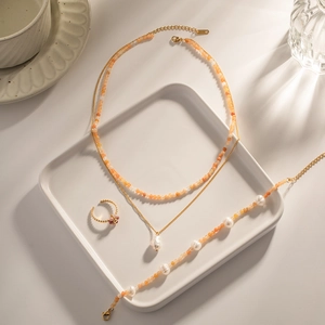 Detail eines 18K vergoldeten Schmucksets mit orangefarbenen Perlen auf weißem Teller