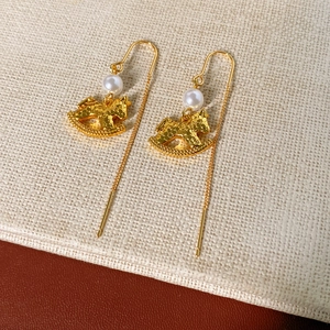 Detail of gold rocking horse earrings with pearls on a textured cream and brown surface