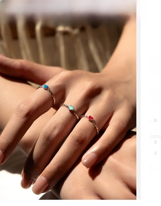 Detail of three twisted silver rings with colorful enamel hearts on a woven background