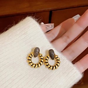 Detail of gold twisted hoop earrings with black teardrop micro-pavé crystal inlay