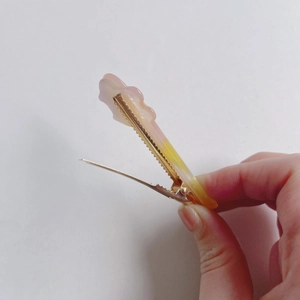 Detail of pink-yellow gradient hair clip with wavy edges and golden metal duckbill clamp