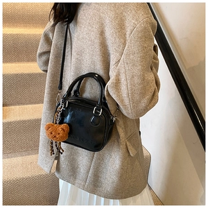Detailed view of black patent leather crossbody bag with teddy bear charm on stairs