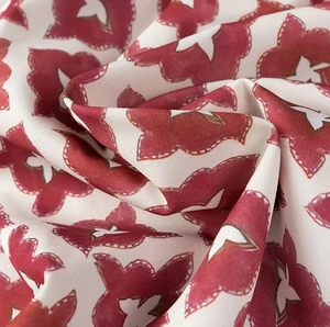 Close-up of red and cream floral silk fabric with artistic wavy patterns and glossy texture