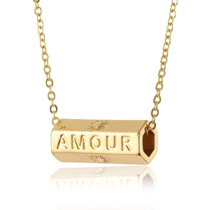 Detail of gold necklace with hexagonal pendant engraved with AMOUR and sun icons