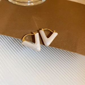 Macro detail of V-shaped gold earrings with white enamel on textured background