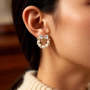 Macro shot of gold bow stud earring with heart zircons and pearls on ear