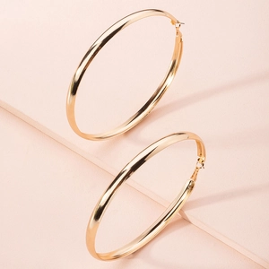 Close-up of large polished gold C-shape hoop earrings on a minimalist pink display stand