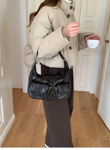 Close-up of a black pleated faux leather baguette bag worn by a model in a casual outfit