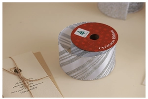 Close-up of silver glitter striped ribbon roll with Merry Christmas tags on beige background