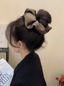 Detail of oversized coffee brown satin scrunchie with silky pleats on a model's hair
