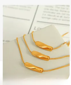 Detailed close-up of a gold snake chain necklace with a sleek twisted cube pendant