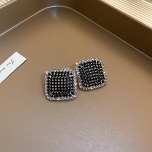 Detailed close-up of square stud earrings with black center gems and white diamond border