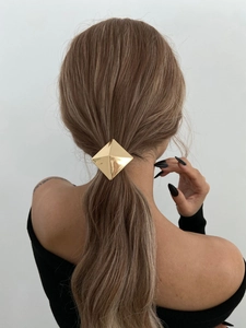Close-up of a geometric gold diamond-shaped metal hair clip on a low ponytail